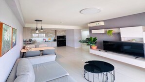Una sala moderna con sofá, mesa de comedor, televisor y cocina al fondo.