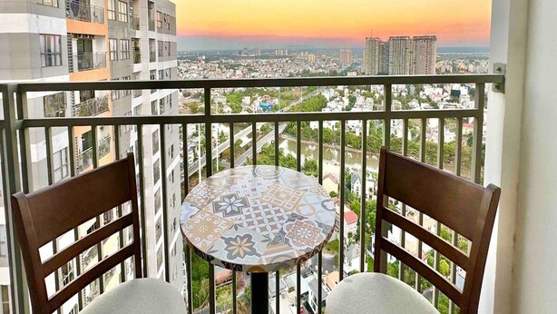 Un balcón con una mesa y dos sillas, con vista a un paisaje urbano al atardecer.