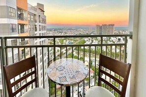Un balcón con una mesa y dos sillas, con vista a un paisaje urbano al atardecer.