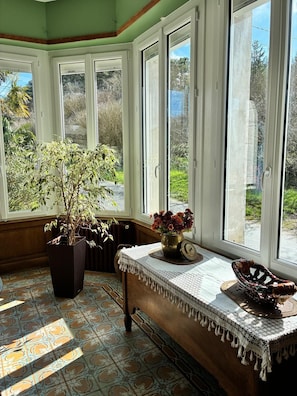 Una habitación con ventanas amplias, una planta en maceta, una mesa con mantel de encaje y un cuenco decorativo.