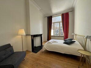 Ein Schlafzimmer mit Bett, Sofa, Lampe, Kamin und einem Fenster mit Vorhängen.