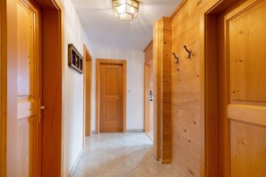 Un couloir avec des portes en bois, un luminaire et un sol carrelé.