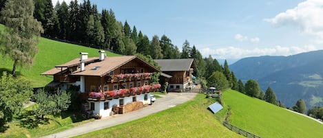 A traditional chalet with a sloped roof, wooden balconies with flower boxes, and a view of the surrounding hills.