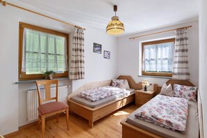 A cozy bedroom with a wooden bed, a chair, a bedside table with a lamp, and a window with curtains. - Farmhouse "Ferienwohnung Pendlhof" with Mountain Views, Shared Garden, and Wi-Fi (Sankt Pankraz)