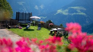 A fenced outdoor area with a trampoline, a table, and chairs, surrounded by a wooden fence and greenery. - Farmhouse "Ferienwohnung Pendlhof" with Mountain Views, Shared Garden, and Wi-Fi (Sankt Pankraz)