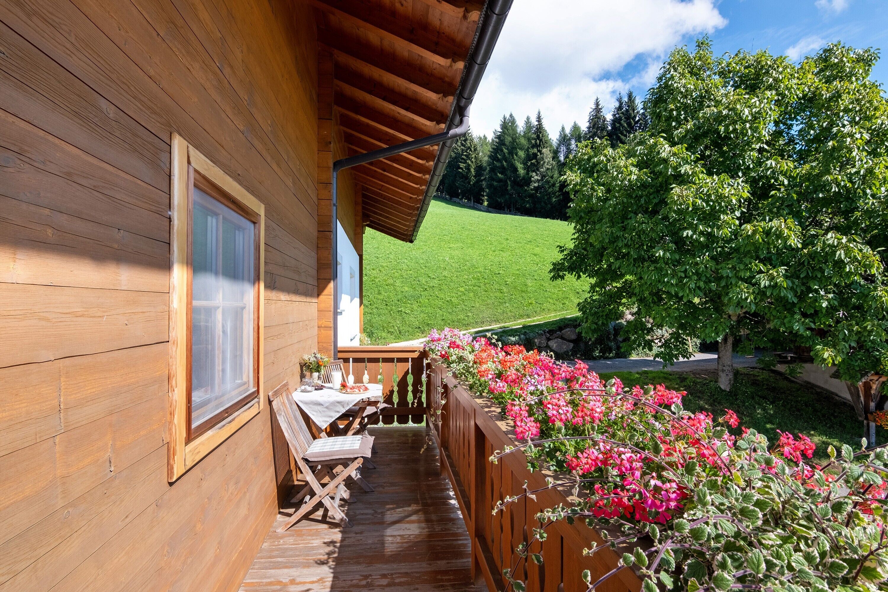 A wooden cabin with a balcony overlooking a green field and a tree.