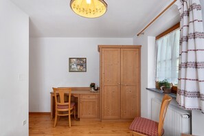 A room with a wooden dining table, a wooden cabinet, a chair, a radiator, and a window with a curtain. - Farmhouse "Ferienwohnung Pendlhof" with Mountain Views, Shared Garden, and Wi-Fi (Sankt Pankraz)