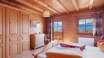Ein Schlafzimmer in einer Holzhütte mit einem Bett, einer Kommode und einem Fenster mit Bergblick.