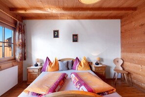 Un dormitorio tipo cabaña de madera con cama, dos mesitas de noche, una silla y una ventana con cortinas.