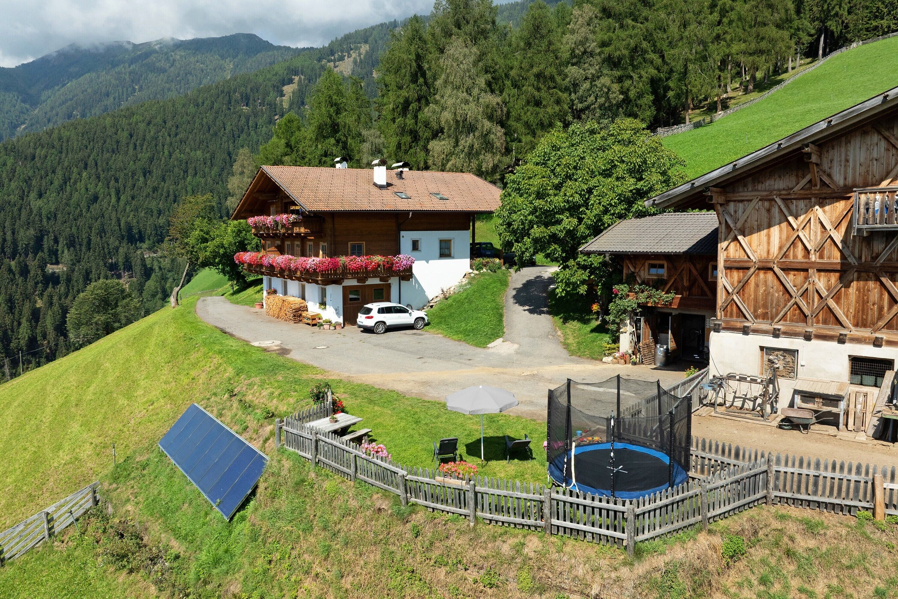 Ein Chalet mit geneigtem Dach, einem Balkon mit Blumenkästen, einer Solaranlage und einem Trampolin.