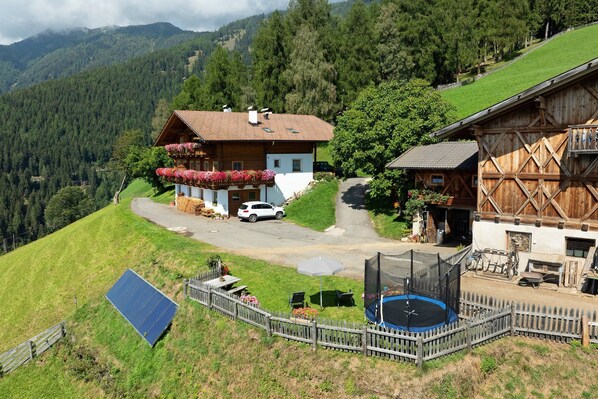 Una cabaña con techo inclinado, un balcón con jardineras y un panel solar, además de un trampolín.