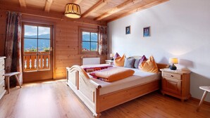 A wooden bedroom with a bed, bedside tables, a window with a view, and a ceiling light. - Farmhouse "Ferienwohnung Pendlhof" with Mountain Views, Shared Garden, and Wi-Fi (Sankt Pankraz)