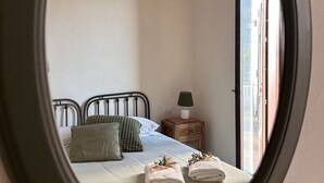 Un dormitorio con cama, almohadas, mesita de noche con lámpara y espejo que refleja la habitación.