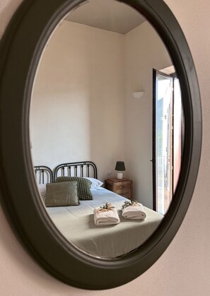 Ein Schlafzimmer mit einem Bett, Kissen, einem Nachttisch mit Lampe und einem Spiegel, der den Raum reflektiert.