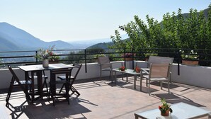 Una terraza con una mesa y sillas, plantas en macetas y vistas a un paisaje montañoso.