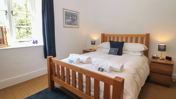 Una camera da letto con un letto di legno, due comodini, una finestra con tende, un quadro appeso al muro e un tappeto blu.