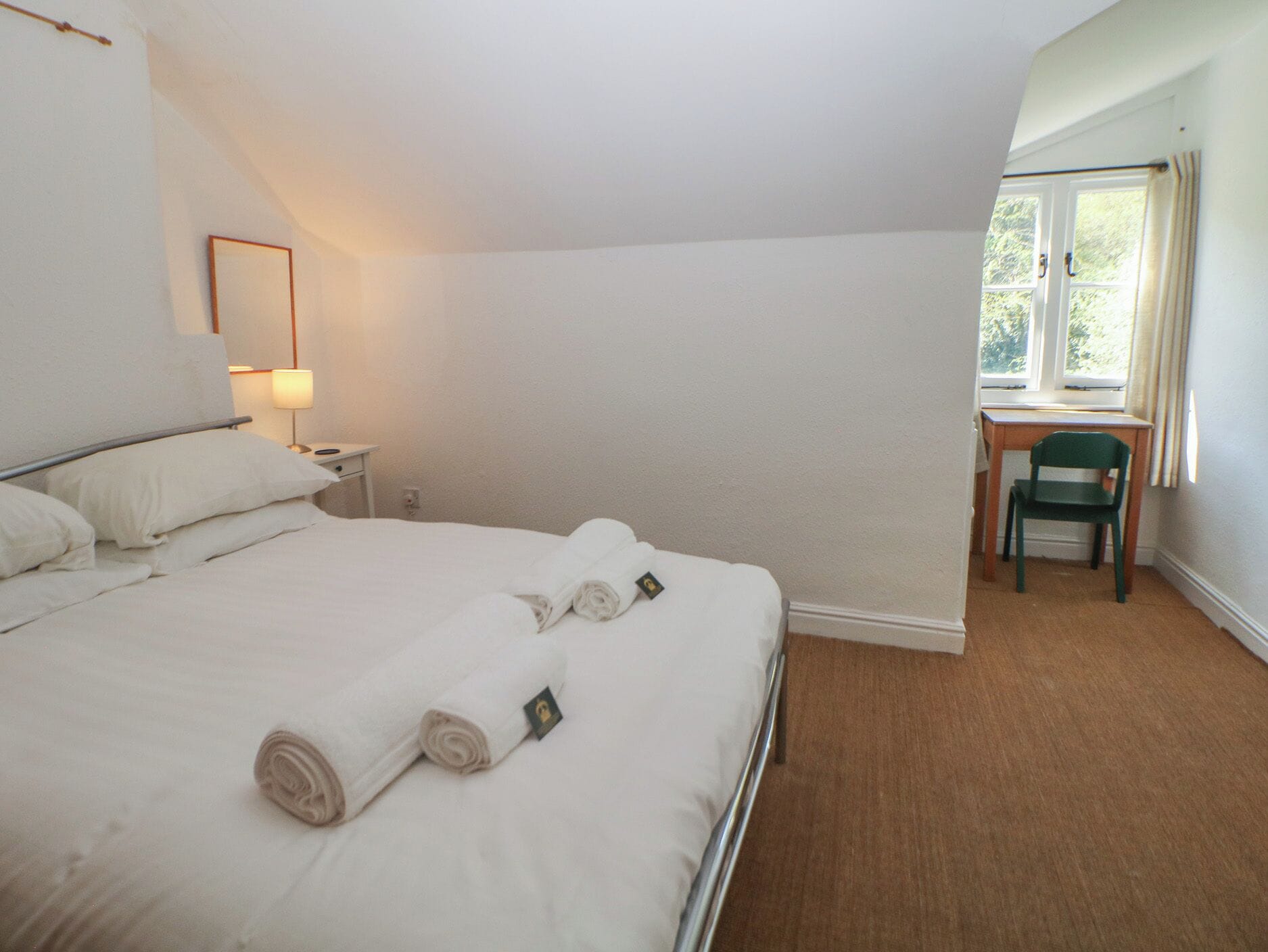 A bedroom with a bed, a desk, a chair, a window, and a lamp.