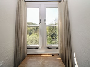 Ein Zimmer mit Fenster, Vorhängen und Blick ins Grüne.