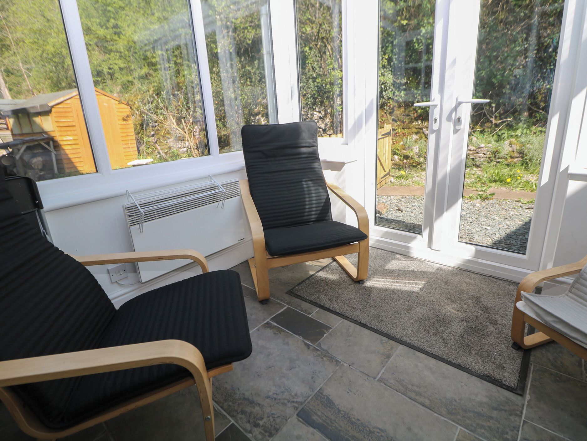 A sunlit room with a large window, a radiator, and two wooden chairs with black cushions.