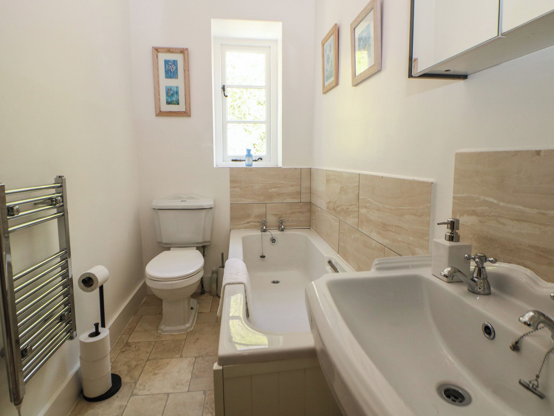 Un baño con inodoro, bañera y lavabo, con una ventana sobre el inodoro.
