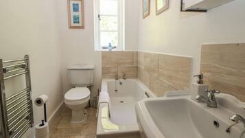 Un baño con inodoro, bañera y lavabo, con una ventana sobre el inodoro.