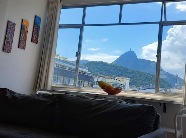 Ein Zimmer mit einem großen Fenster, einer schwarzen Ledersofa und drei farbenfrohen Bildern an der Wand.