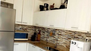 Una cucina con mobili bianchi, frigorifero in acciaio inossidabile, microonde, macchina da caffè e lavastoviglie Samsung.
