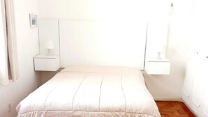 Una camera da letto con un letto, pavimento in parquet di legno, un condizionatore d'aria bianco e comodini con lampade.