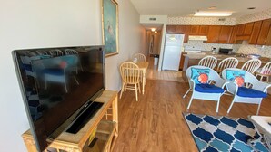 A living room with a flat-screen TV, wooden chairs, a dining table, and a kitchen in the background. - 10% off 3-7 nights through Dec. 1BR 1BA OF condo. Outdoor pool. Cozy getaway. (North Myrtle Beach)