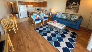 A compact living space with a kitchenette, a dining area with wicker chairs, a blue sofa, and a patterned rug. - 10% off 3-7 nights through Dec. 1BR 1BA OF condo. Outdoor pool. Cozy getaway. (North Myrtle Beach)