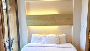 A hotel room with a bed, a wooden headboard, and a glass door. - Coconut Studio Aonang (Krabi)
