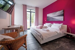 Ein Schlafzimmer mit einem Bett, einem Schreibtisch, Korbstühlen, einem Fenster mit Vorhängen und einer rosafarbenen Wand.