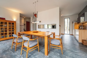 A modern kitchen with a wooden table and chairs, a built-in oven, and a large window. - Modern vacation home in Karlshagen on Usedom with sauna, close to the beach (Karlshagen)