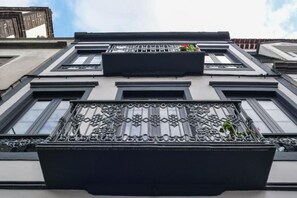 Eine Gebäudefassade mit einem Balkon, verziert mit aufwendigen Metallgeländern und einer Blumenkiste.