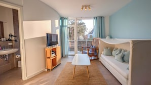 A modern living room with a sofa, a TV, a small table, and a balcony with curtains. - 2-room apartment in Karlshagen on Usedom with terrace, close to the beach (Karlshagen)