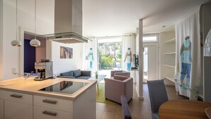 Eine moderne Küche mit Kochinsel, eine Essecke mit Tisch und Stühlen sowie ein Wohnbereich mit Sofa und Sessel.