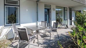 Eine Terrasse im Freien mit Tisch und Stühlen, eine Tür mit der Aufschrift 'Kajute' und Blick auf die Straße.