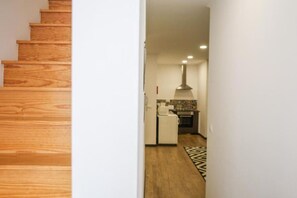 Eine Holztreppe führt zu einer Küche mit einer gefliesten Spritzschutzwand und einer Pendelleuchte.