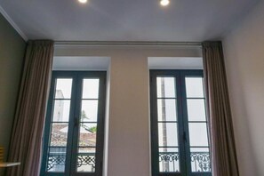 Ein Zimmer mit zwei großen Fenstern, einem Balkon mit Metallgeländer und einer Decke mit Einbuchtungslampen.