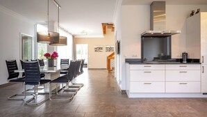 Una cocina moderna con armarios blancos, una campana extractora de acero inoxidable y un comedor con mesa de vidrio y sillas negras.