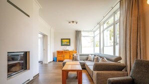 Una sala de estar con un sofá, una mesa de centro de madera, un televisor y un ventanal con cortinas.