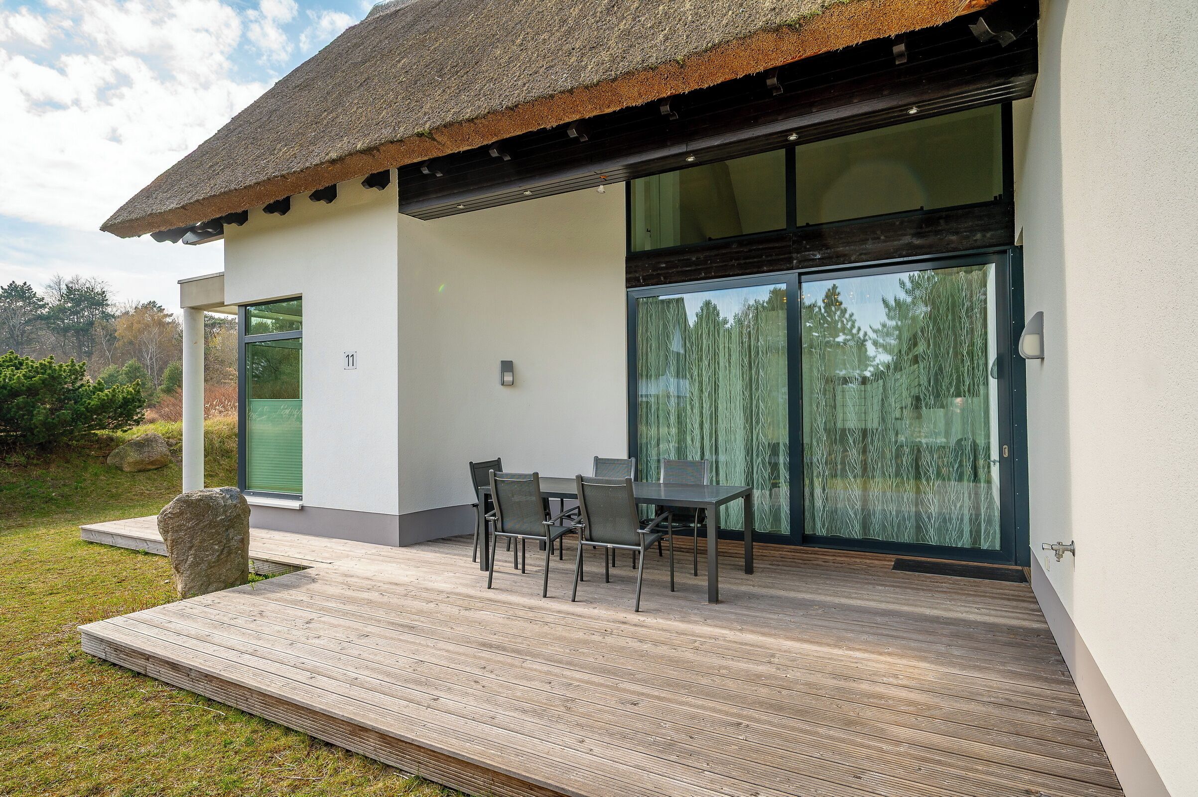 Ein modernes Haus mit Terrasse, einem Esstisch und Stühlen sowie einer großen Glasdoor.