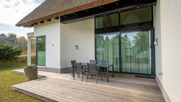 Ein modernes Haus mit Terrasse, einem Esstisch und Stühlen sowie einer großen Glasdoor.