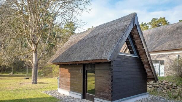 Una pequeña cabaña de madera con techo de paja, una puerta y una ventana.