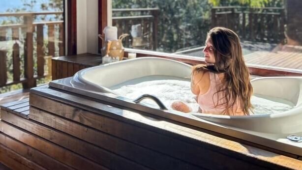 A person in a hot tub with a view of a wooden deck and trees.