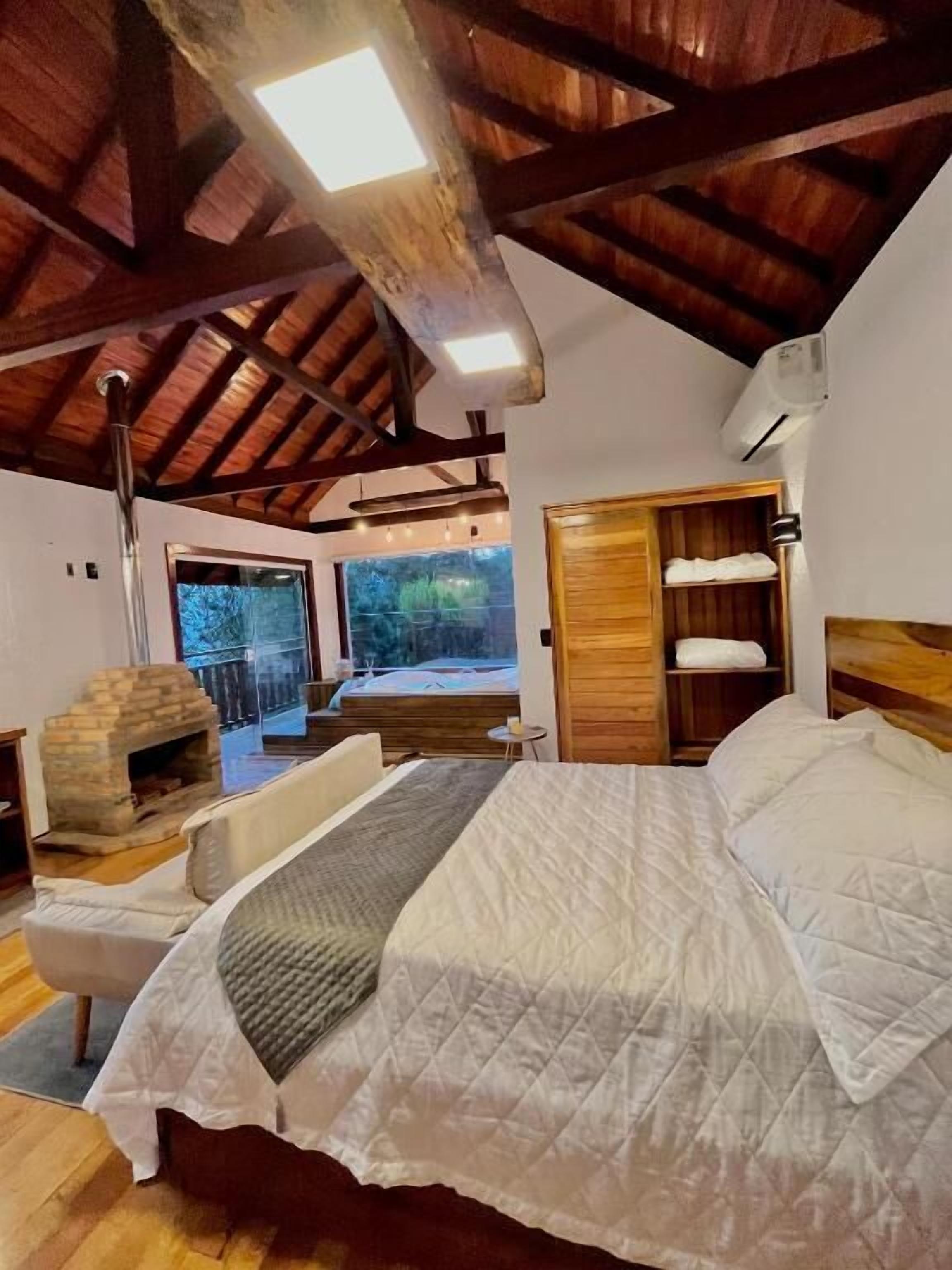 Une chambre avec un plafond en bois, une cheminée, un lit avec une literie blanche et une vue sur l’extérieur.