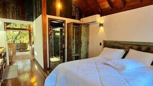 A spacious bedroom with a large bed, wooden ceiling beams, and a view of the outdoors.