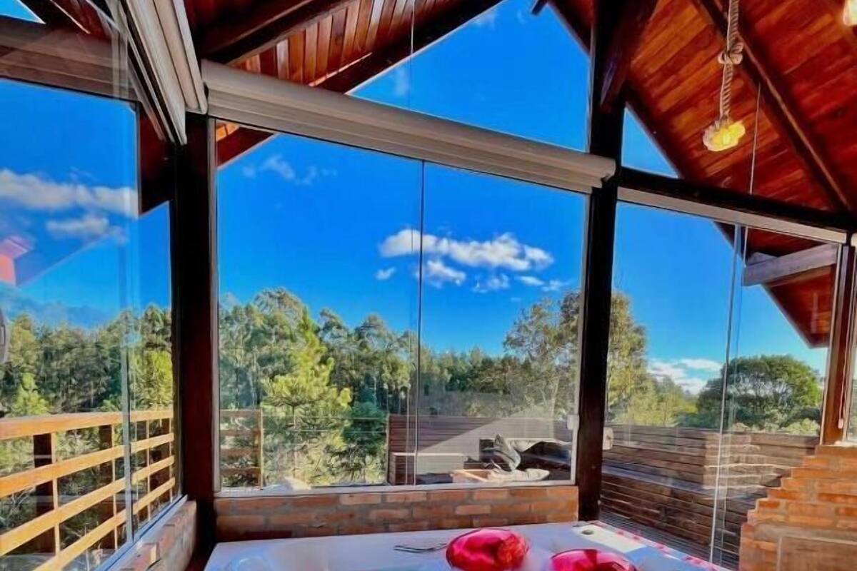 A hot tub with rose petals and a bottle of wine, surrounded by a wooden deck and a view of trees.