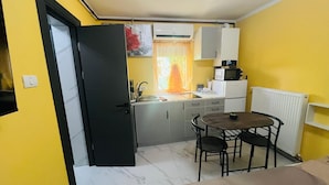 A compact kitchen with a dining area, a white refrigerator, a microwave, and a window with curtains.