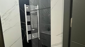 A modern bathroom with a glass shower enclosure, a white marble wall, and a built-in towel rack.
